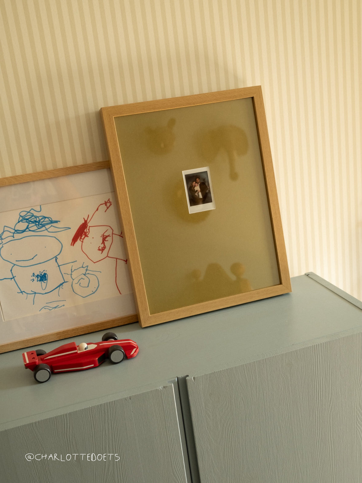 Eiken lijst met een olijfgroen passe-partout en een polaroid in een kinderkamer, naast een kindertekening