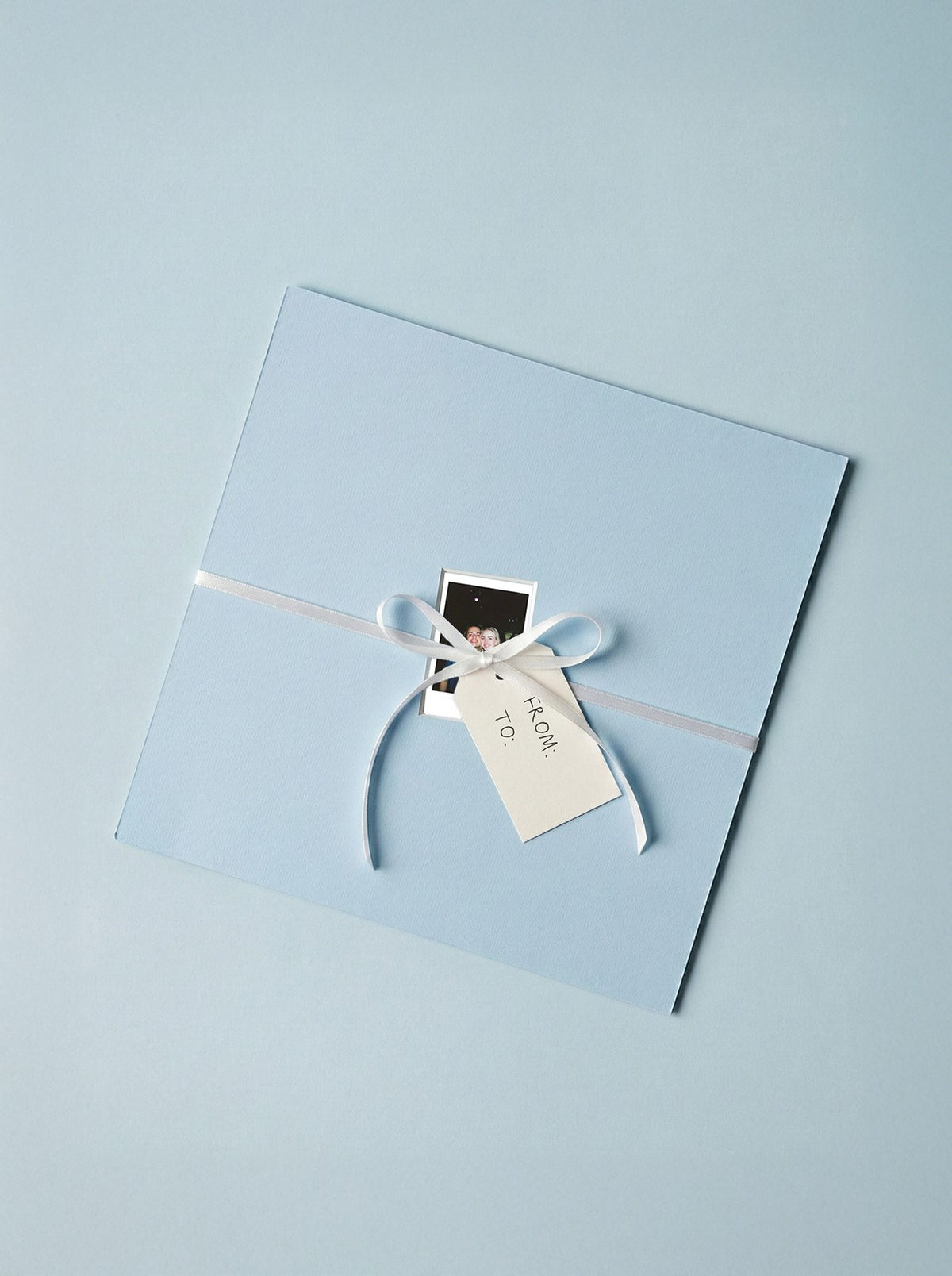 Lichtblauwe passe-partout met een polaroid, ingepakt als cadeau met een wit lintje en kaartje