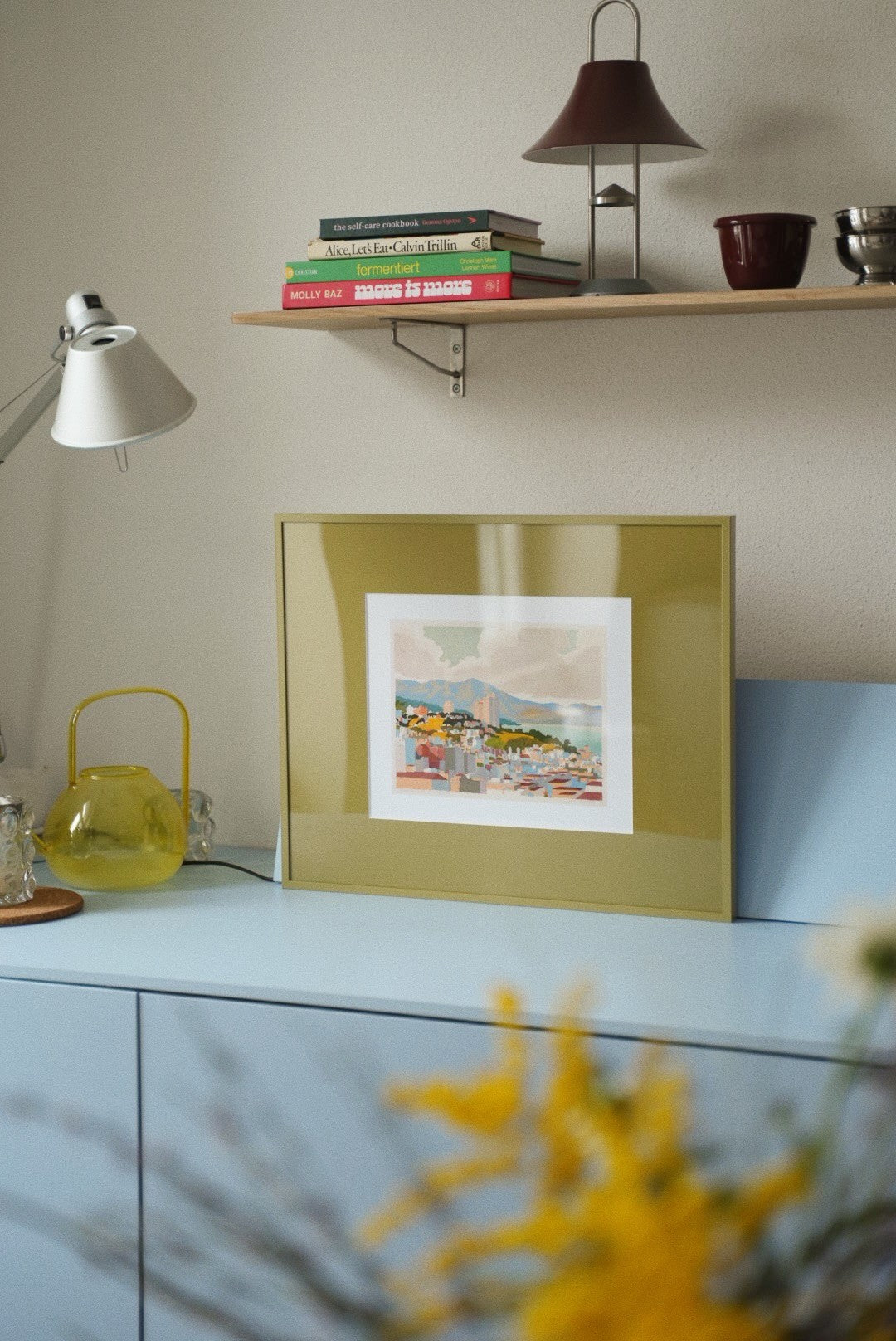 Olijfgroene wissellijst met een print op een lichtblauwe kast