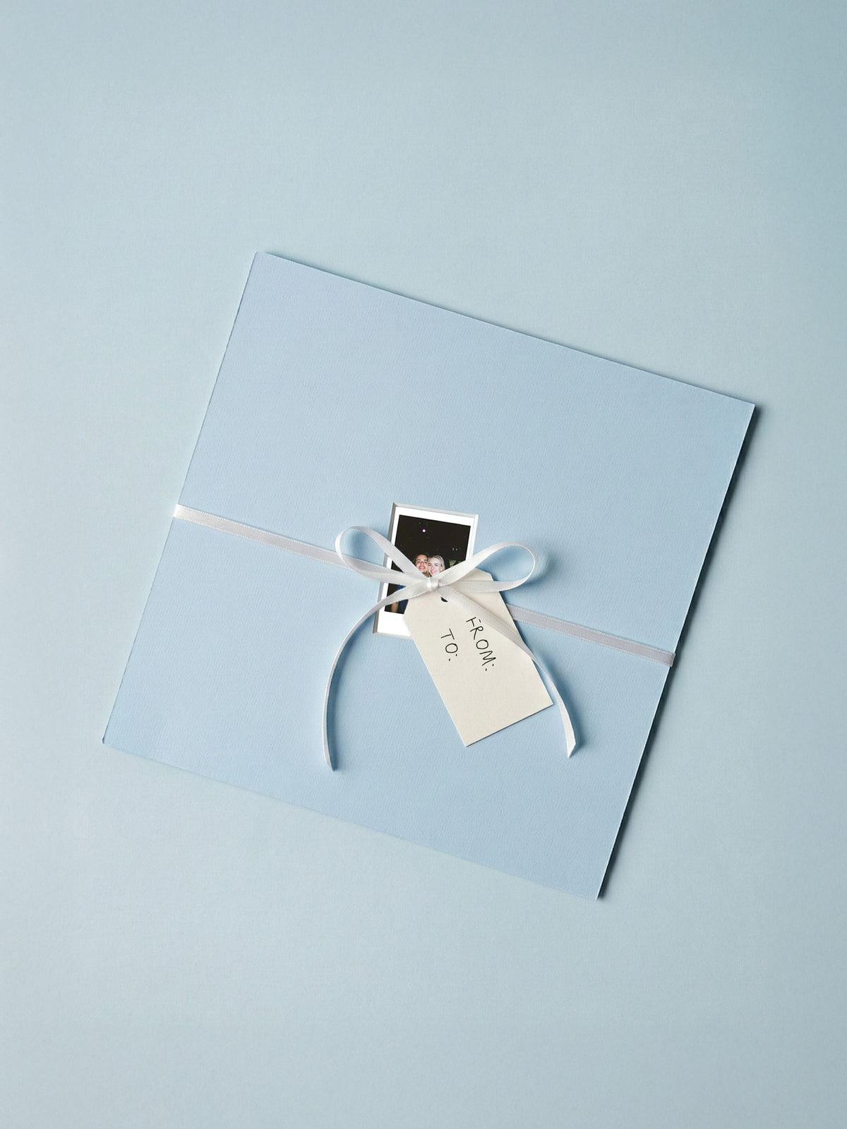 Hellblaues Passepartout als Geschenk verpackt mit Schleife, Polaroid und Geschenkanhänger