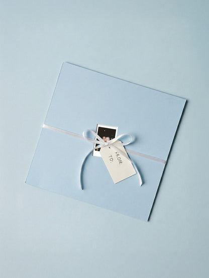 Hellblaues Passepartout als Geschenk verpackt mit Schleife, Polaroid und Geschenkanhänger